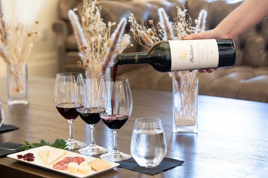 Pouring red wine into glasses with a plate of charcuterie