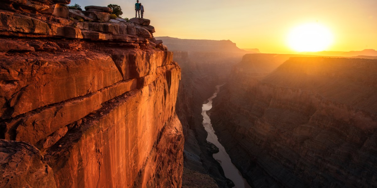 the sun rests over the horizon as people look on from the edge of the grand canyon