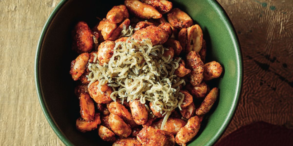 Mister Jiu's in Chinatown Spicy Crispy Peanuts pictured in a green bowl topped with fried anchovies.