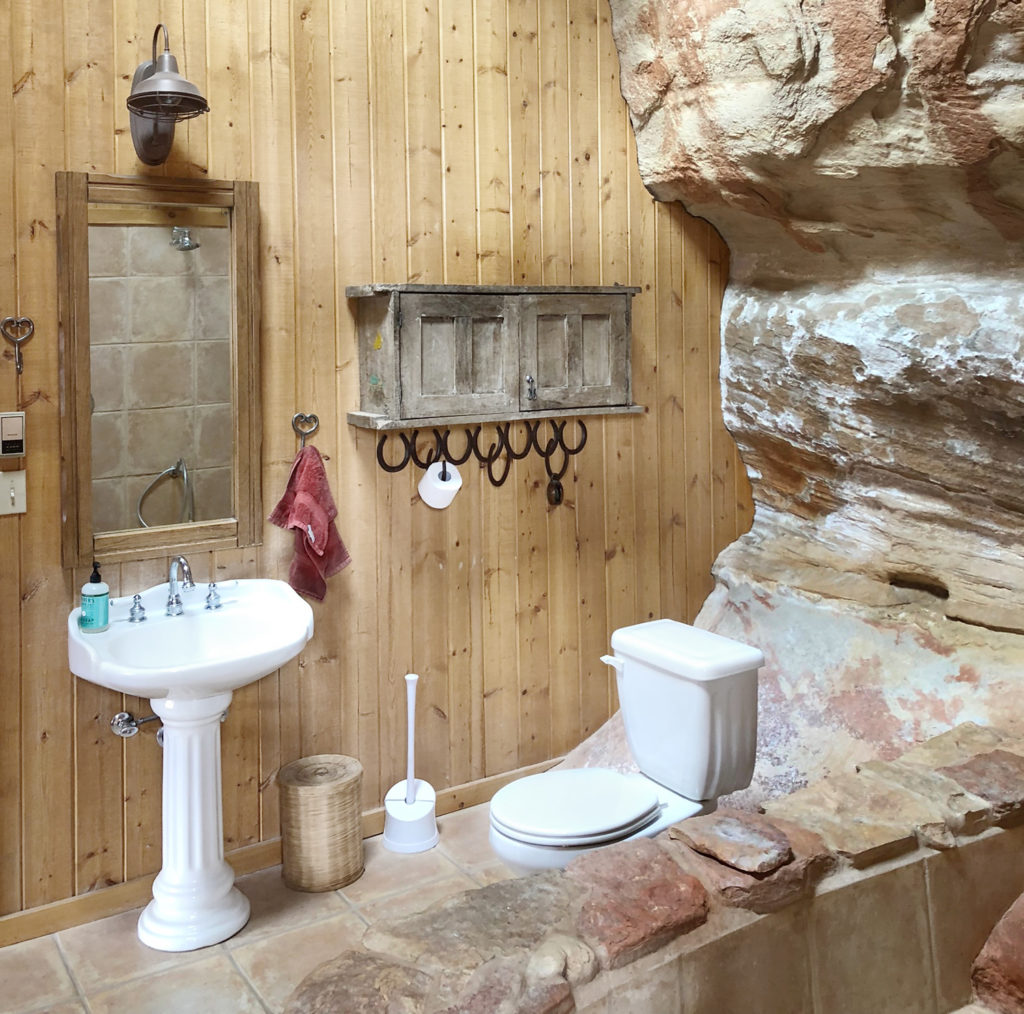 bathroom sink and toilet inside cave walls with wood wall on one side
