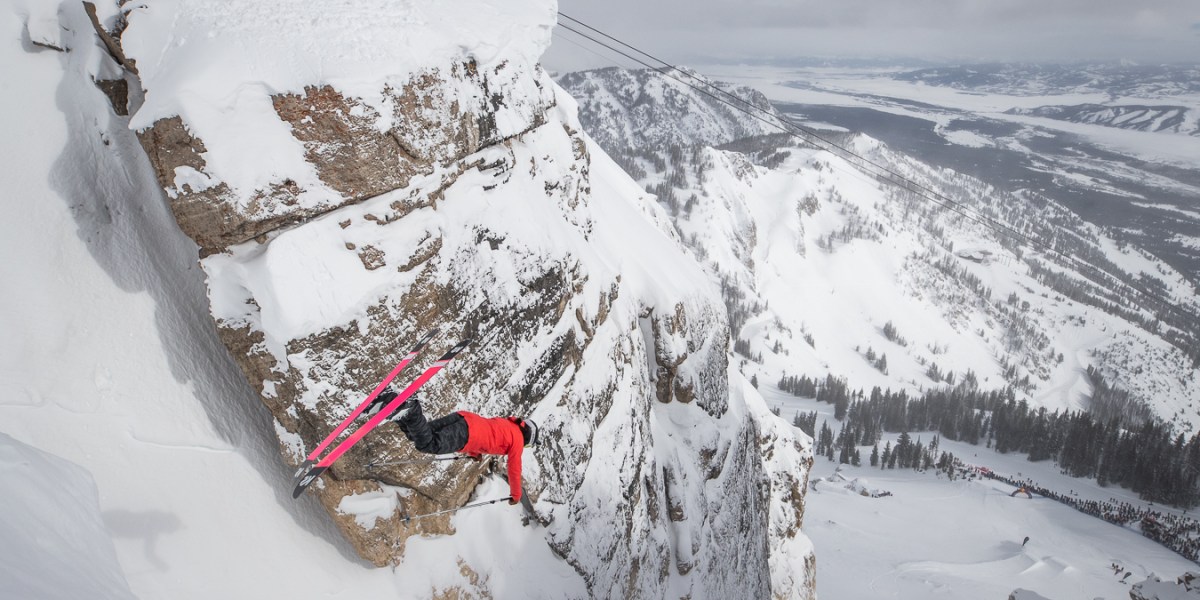 Skiier about to land flip into narrow ski run next to rock walls