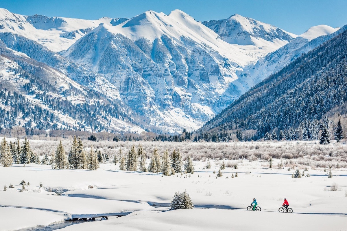 People fat tire biking through a valley with giant mountains in the background in snowy Telluride