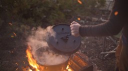 dutch oven being opened over roaring fire in the woods