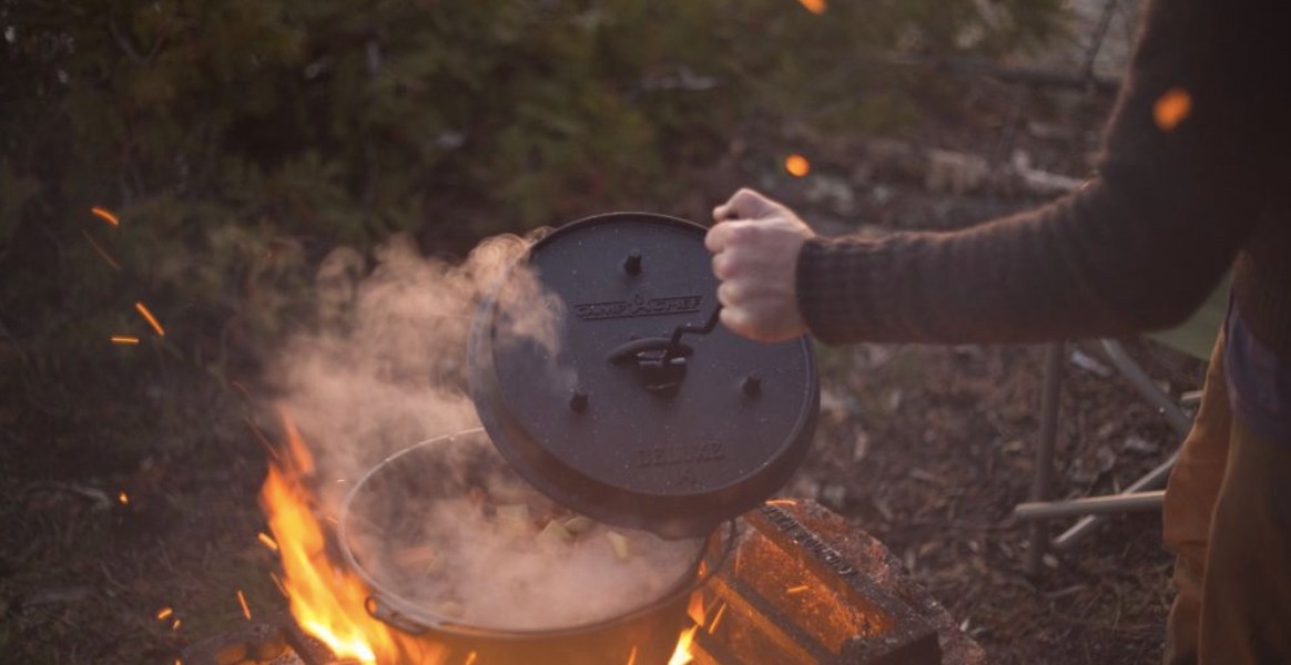 dutch oven being opened over roaring fire in the woods