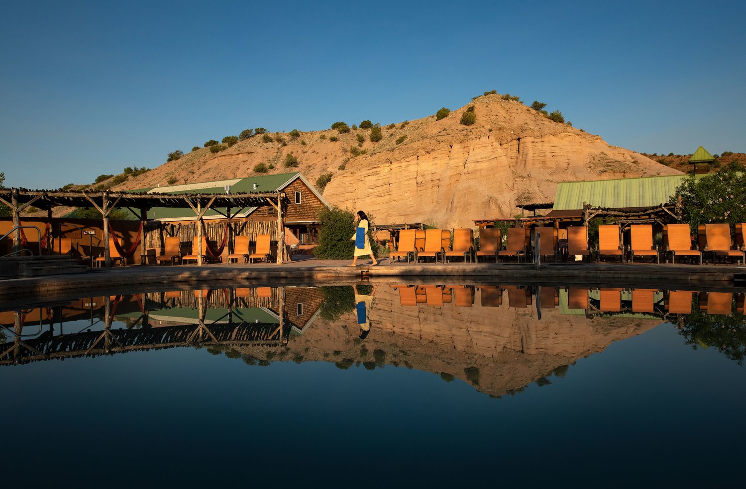 Woman walking across deck at the pool at Ojo Caliente with red rock mountain in background