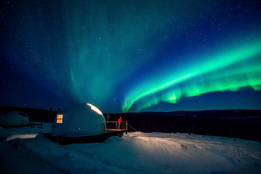 Man standing on deck of a pod room at Borealis Basecamp watching northern lights
