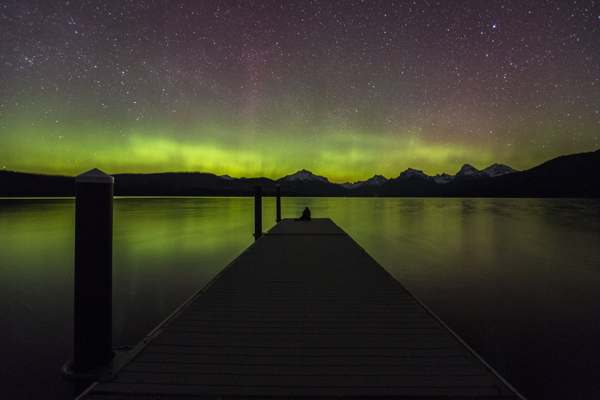 Person at end of dock watching northern lights in Glacier National Park