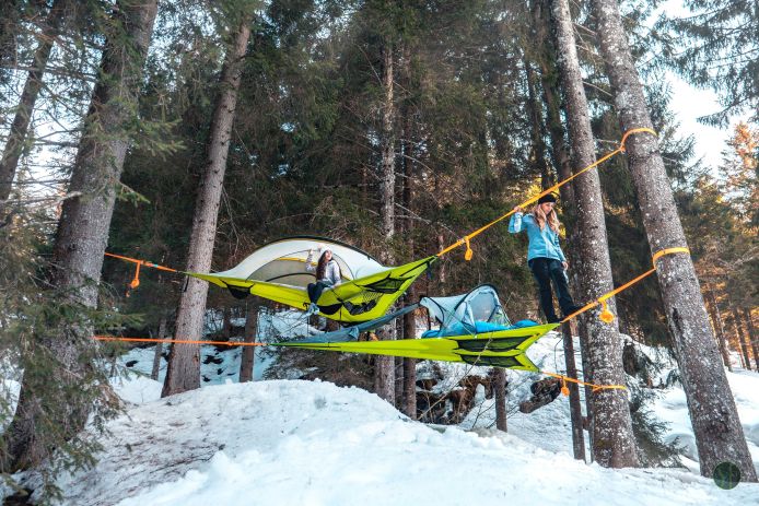two tents suspended in air over forest floor covered in snow
