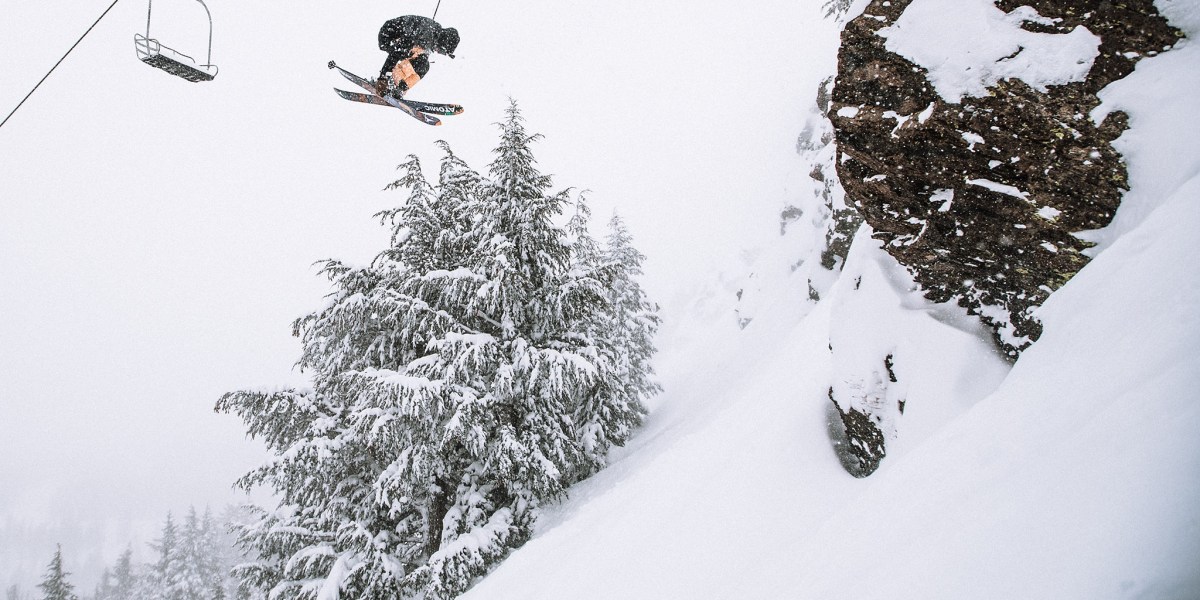Skiers doing a flip while skiing at Mammoth slopes covered in snow with grey skies and snow falling