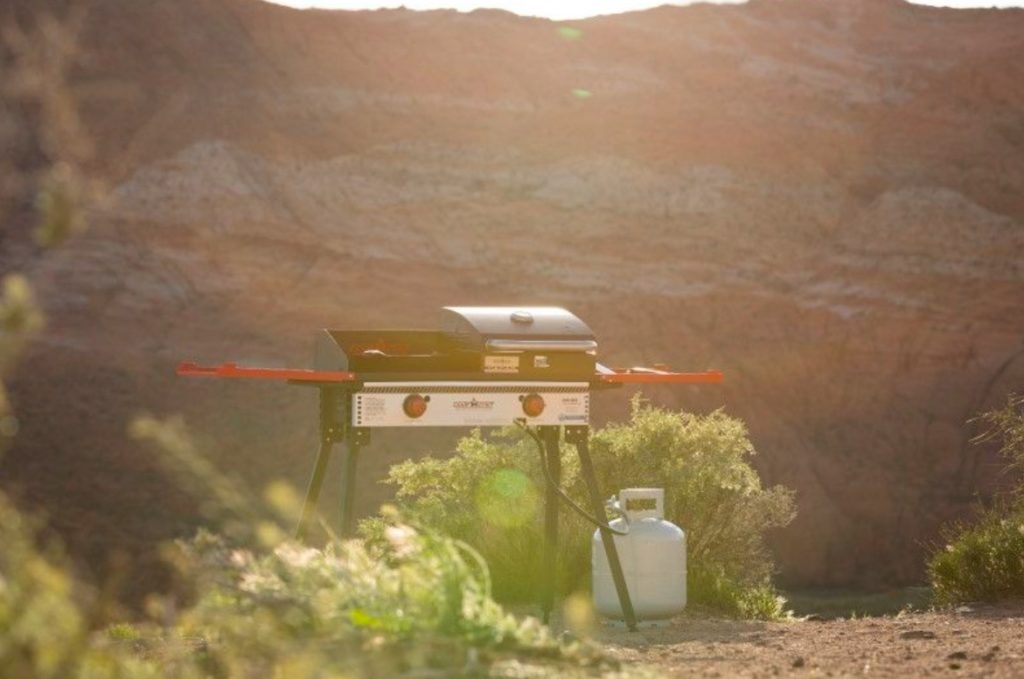 two burner stove with grill accessory and propane tank set up in canyon