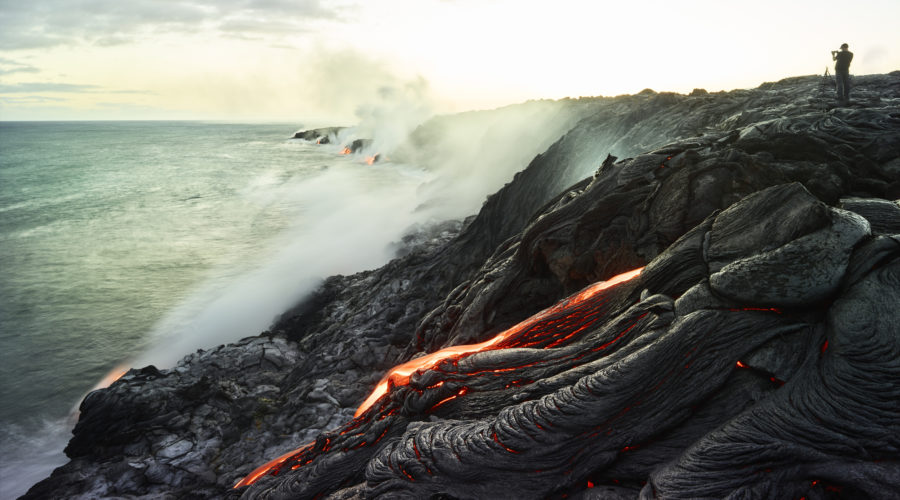 Man standing on volcano taking photo of ocean at Hawaii Volcanoes National Park, a UNESCO World Heritage Site