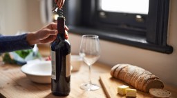 Person opening a bottle of wine on a wooden countertop.